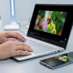 Personne tapant sur un PC portable HP visionnant une vidéo, avec un smartphone affichant un transfert/aperçu à côté sur un bureau épuré.