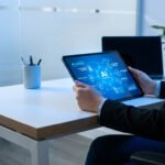 Personne en tenue professionnelle utilisant une tablette tactile avec une interface graphique d'IA au bureau.